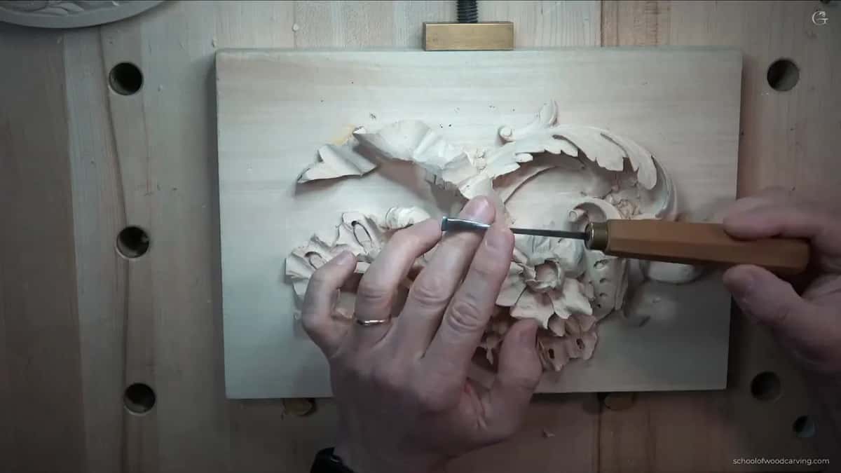 Tool held above a carved panel of leaves and scrolls.