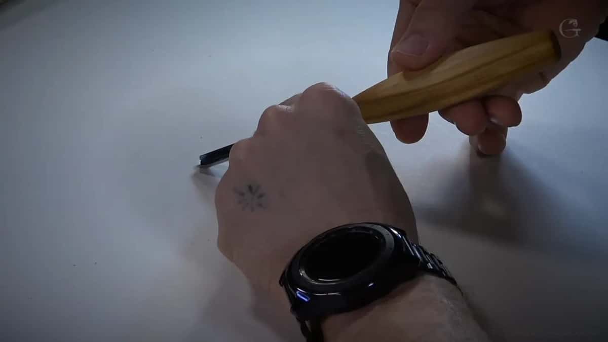 Hand gripping the pale handle with a watch on the wrist, blade pointing away from the camera.