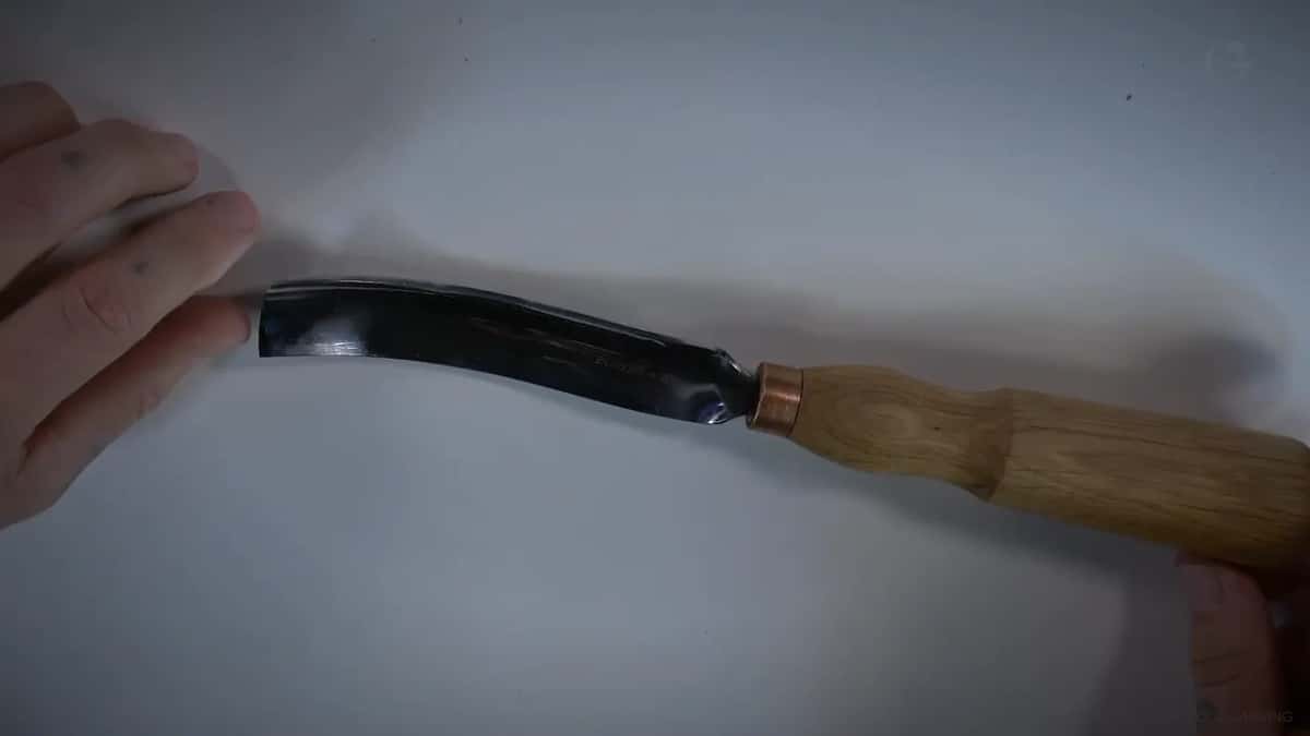 Long bent gouge laid full length across the bench, the curve of the blade clear from handle to edge.