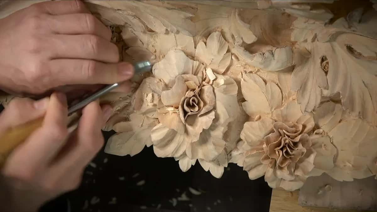 Holding a bent tool with both hands among the carved leaves under a flower