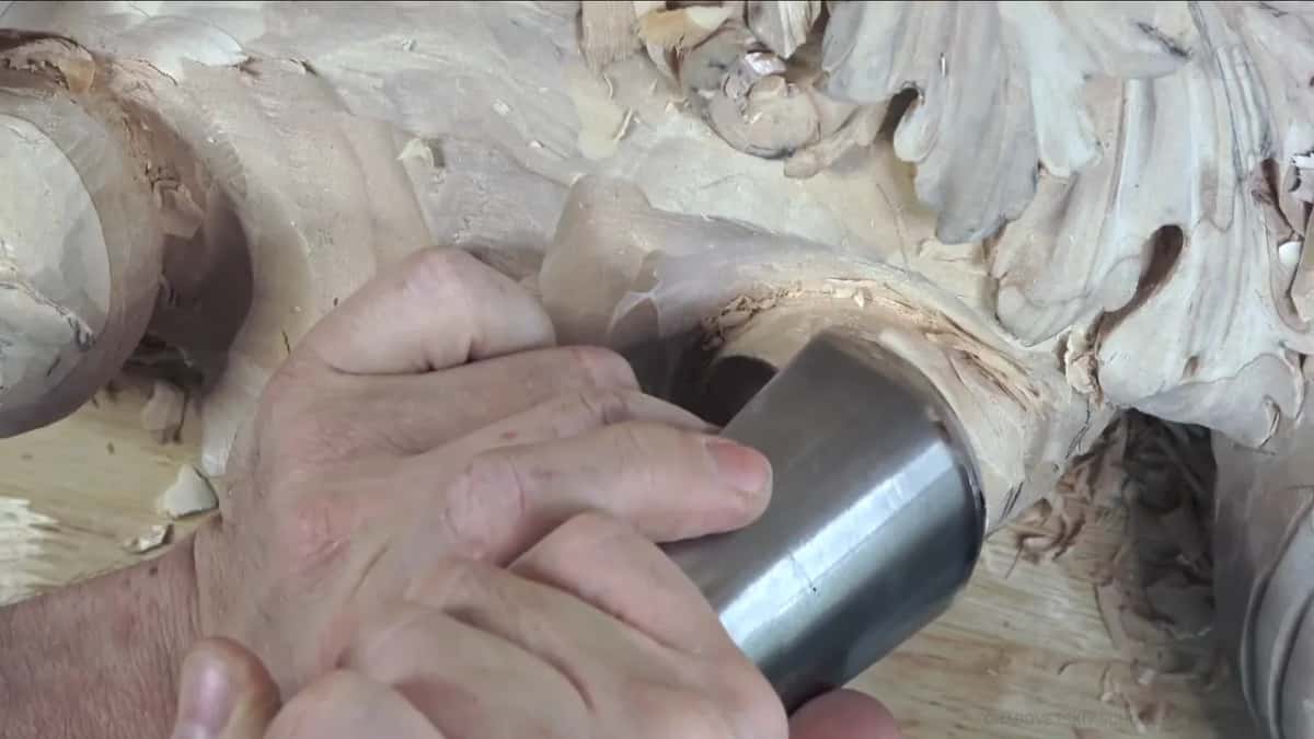 Big gouge with a metal ferrule pressed to the barrel, both hands on it and chips on the bench.