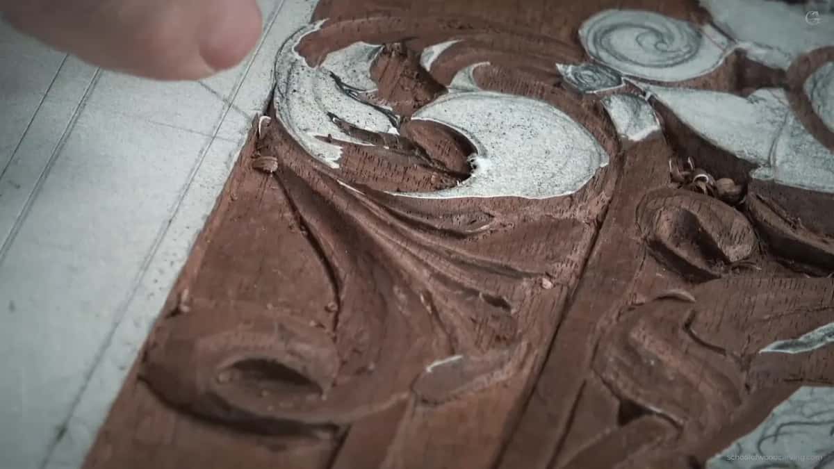 Hand coming in from the top left corner, the carved scroll below it lit hard from one side.
