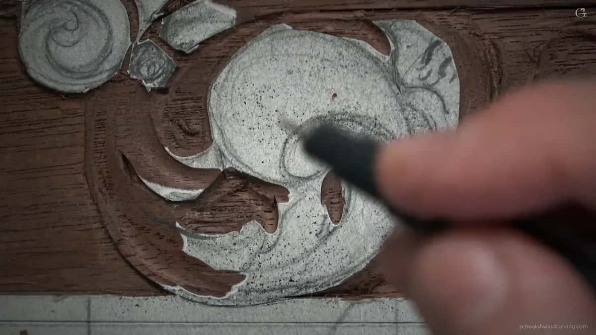 Marker tip against carved walnut, redrawing a separation line that disappeared earlier under the chips while he worked on it.
