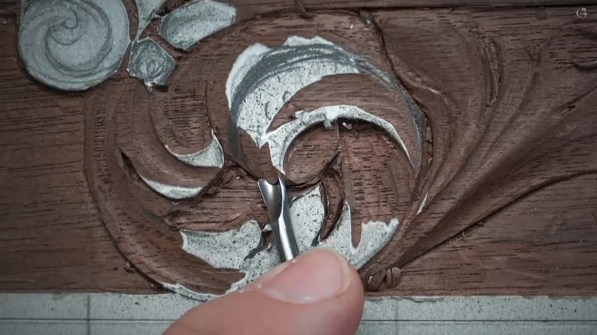 Narrow gouge working the eye of the scroll, a thumb braced underneath, and the hollow already reading quite dark.