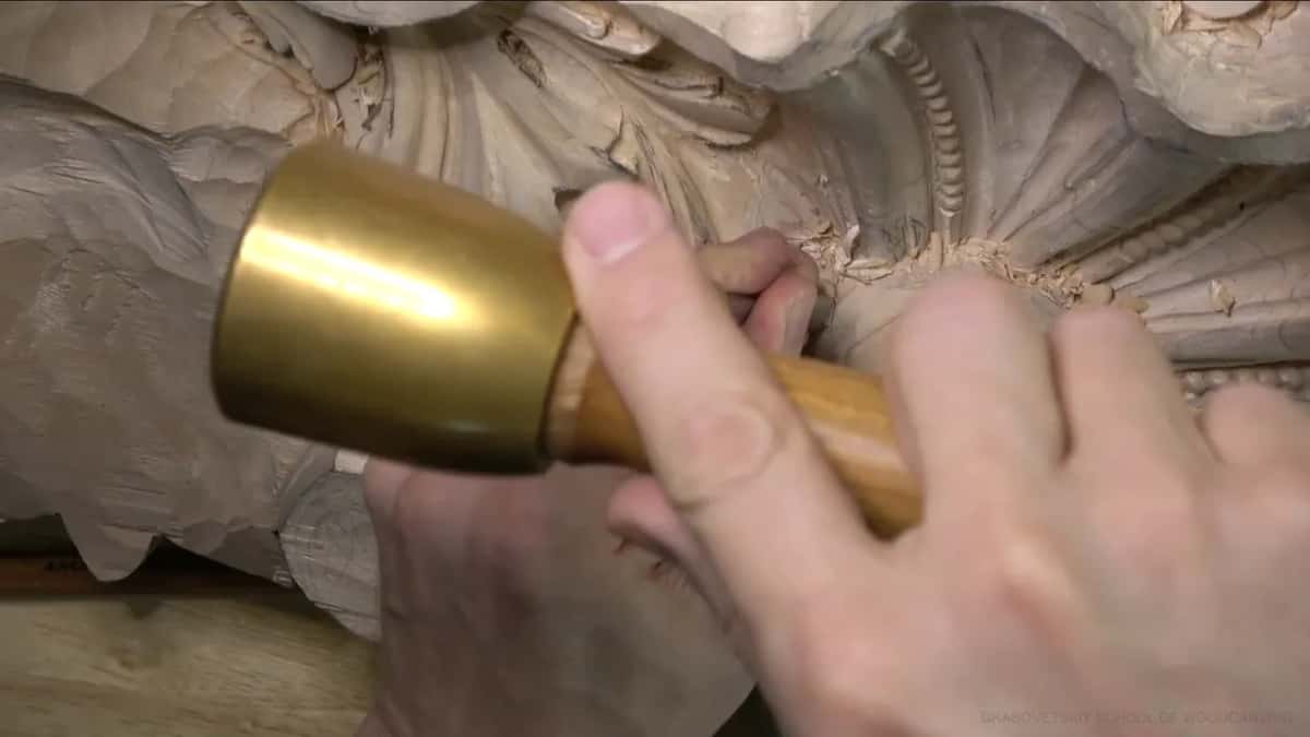 Brass mallet with a pale handle, held above the shell.