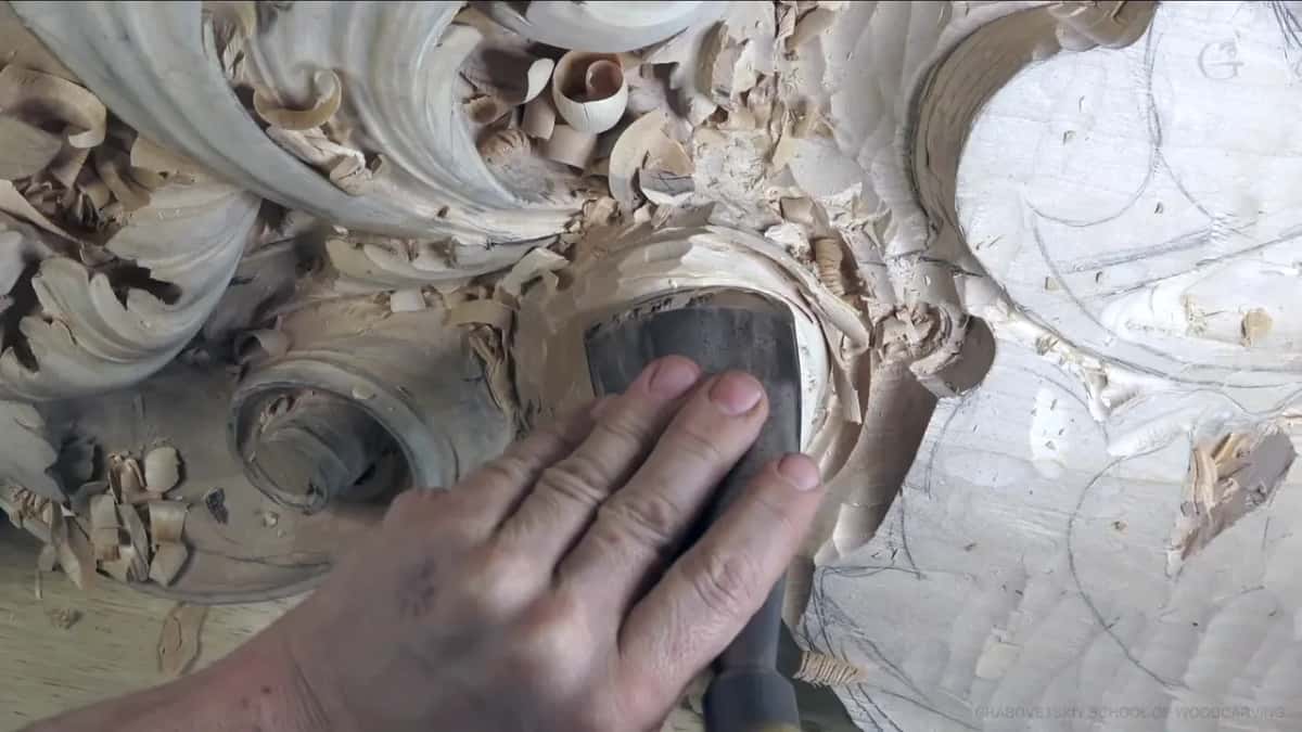 Broad gouge pressed into a curved hollow, one hand on top and shavings heaped around the cut.