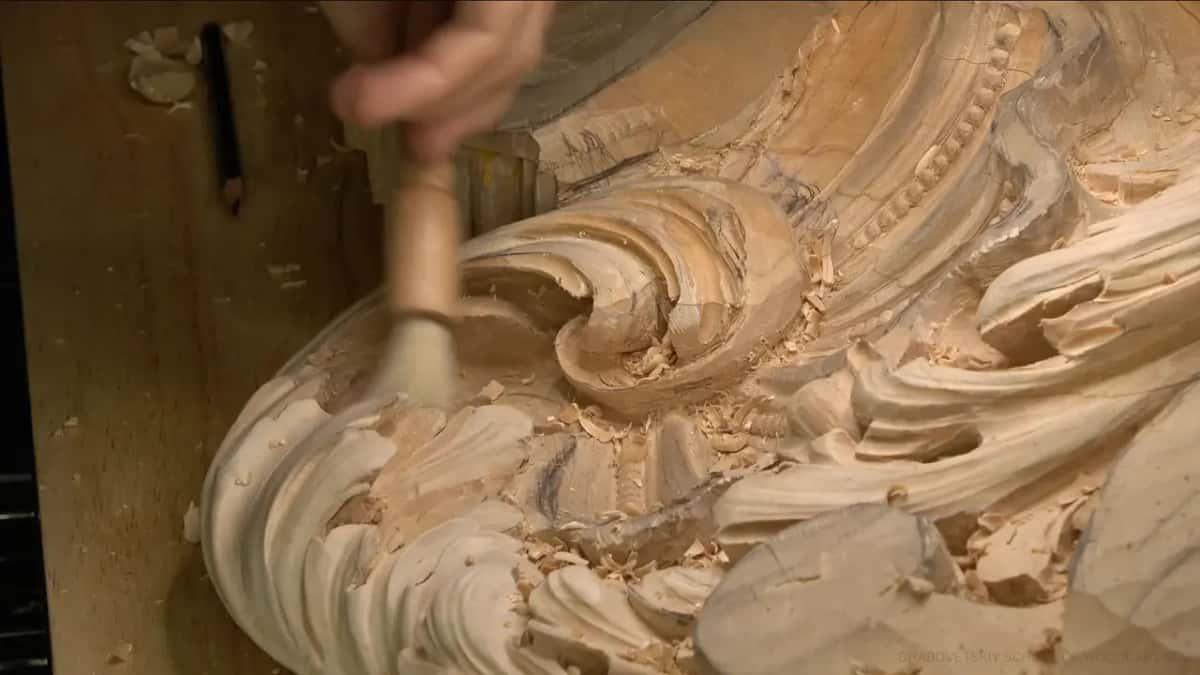 A round brush sweeps the chips out of the curl, and a pencil lies on the bench nearby.