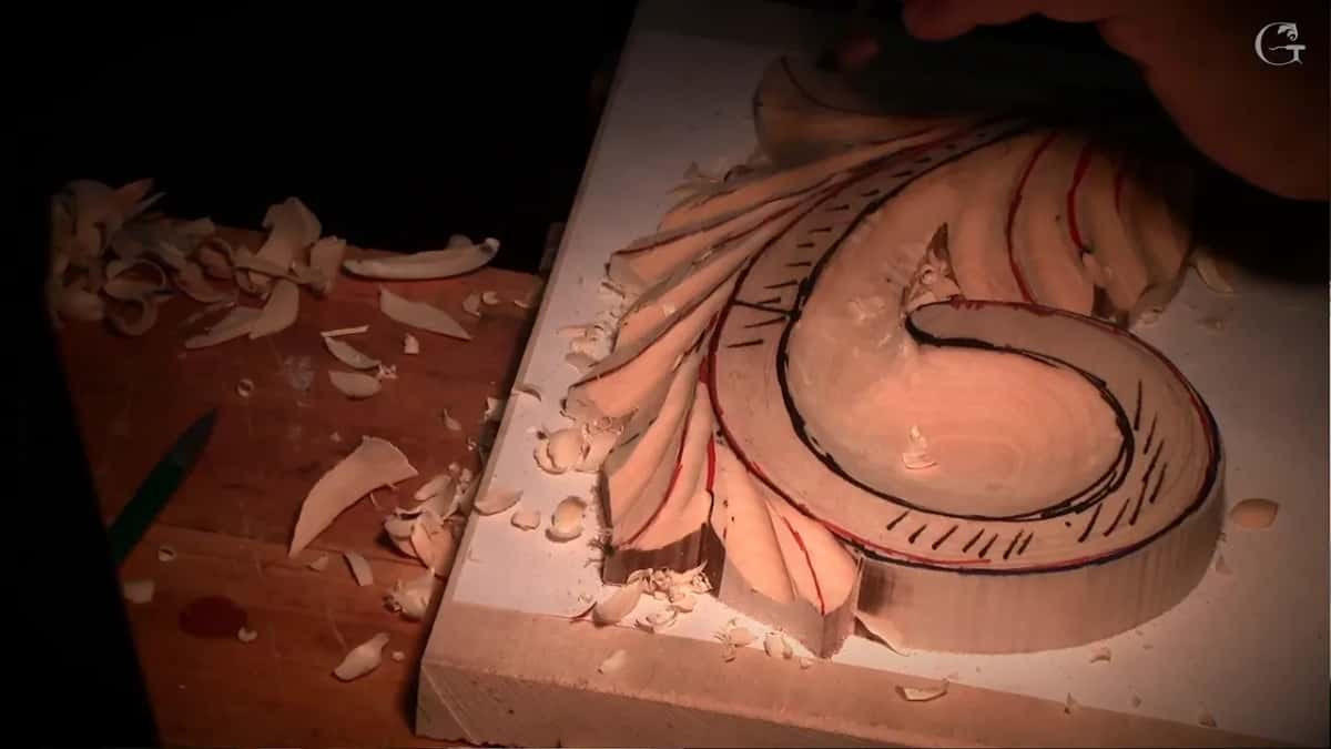 Carved scroll under warm raking light, marked in black, chips all round it