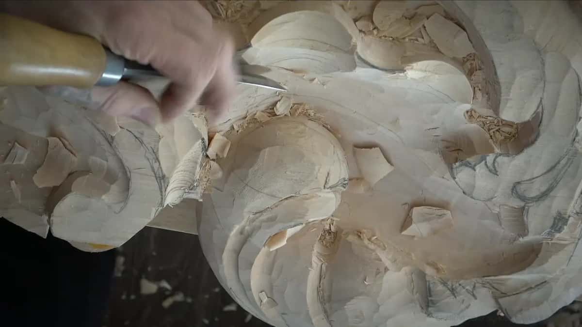 From the top left, a hand drives a gouge toward pencil lines on the half carved shell below