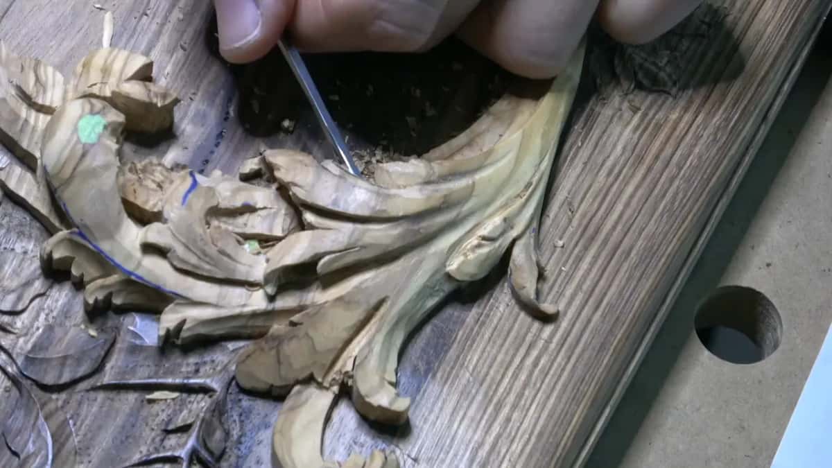 Thin straight tool dipping into a dark hollow behind the top of the acanthus