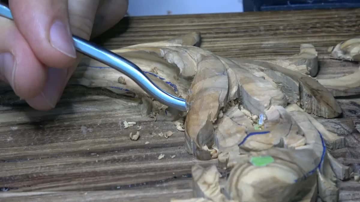 Close side view of a bent silver gouge sliding under an olive leaf drawn with blue pen