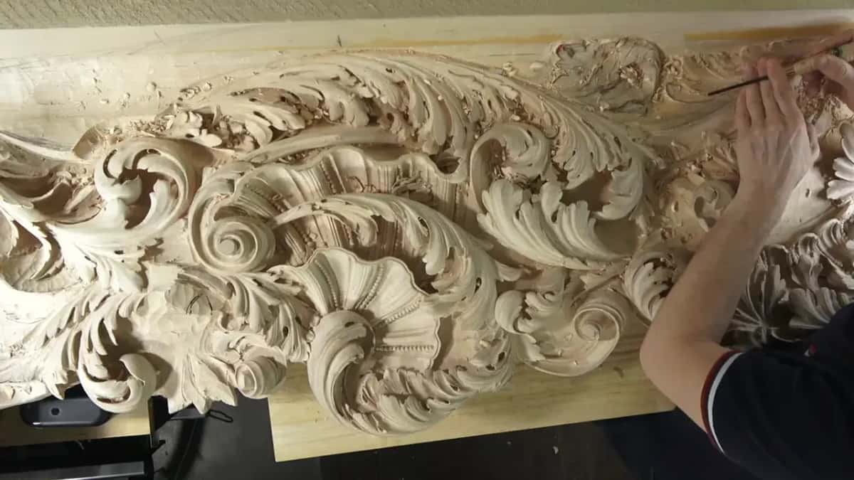 Overhead view of the carved ceiling board, with one hand working a thin tool at its right end.