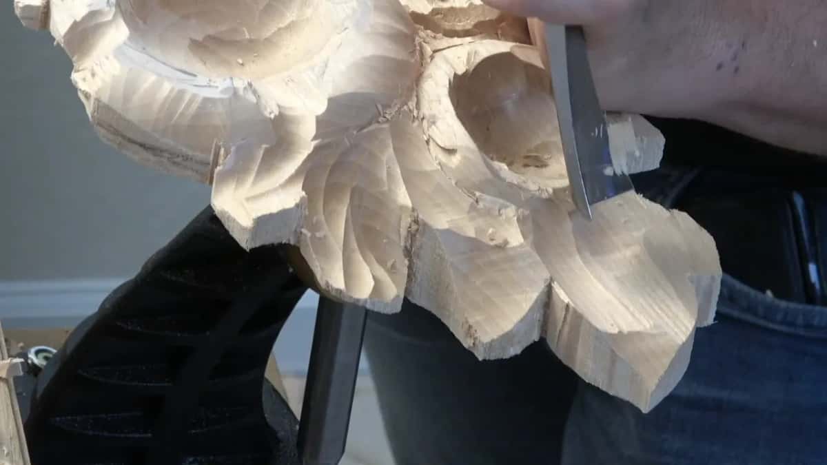 Gouge working the side of the panel where the leaves meet a flower, seen edge on