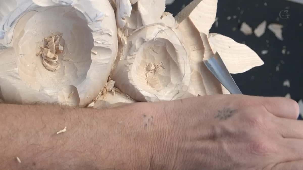 Forearm across the panel, a blade angled into the smaller flower behind it
