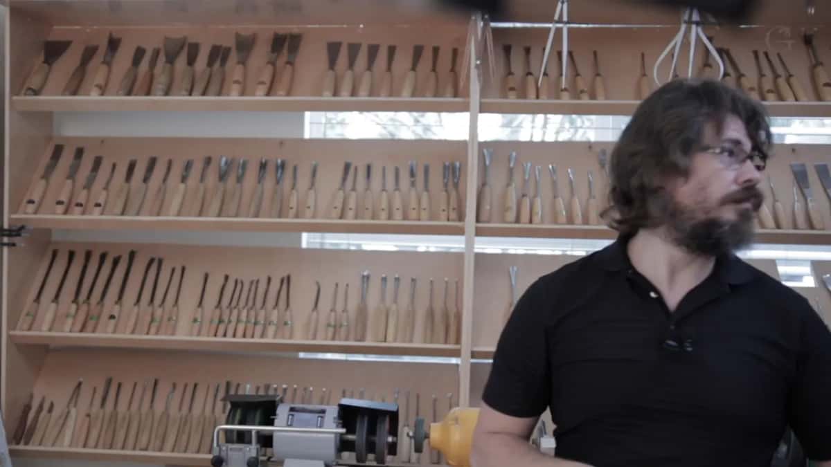 Four shelves of gouges and chisels on the shop wall behind the bench