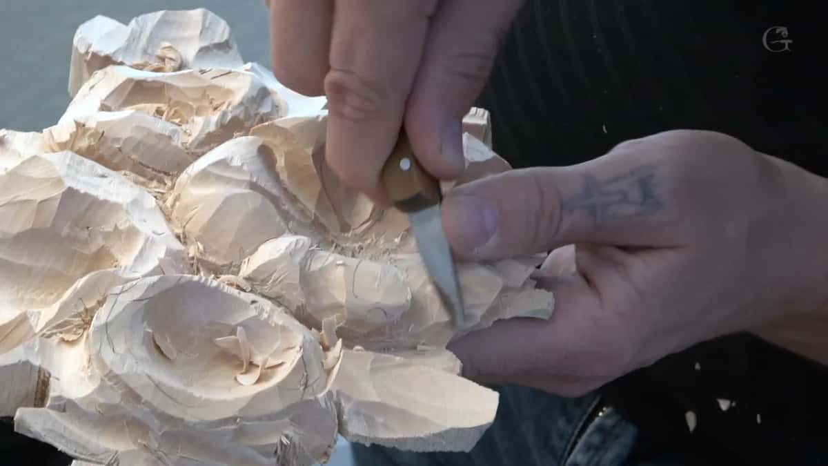 Small carving knife with a brass rivet through its handle, gripped in both hands while the blade works a petal edge
