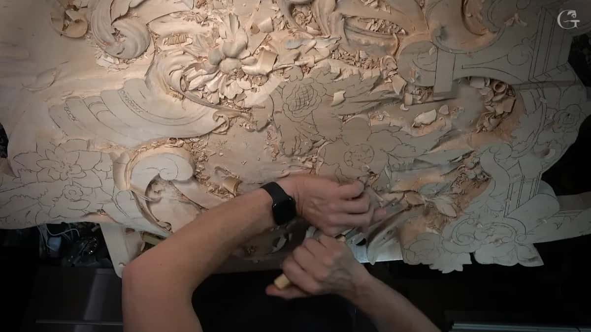 Overhead view of the whole panel, both hands at a gouge among roughed leaves