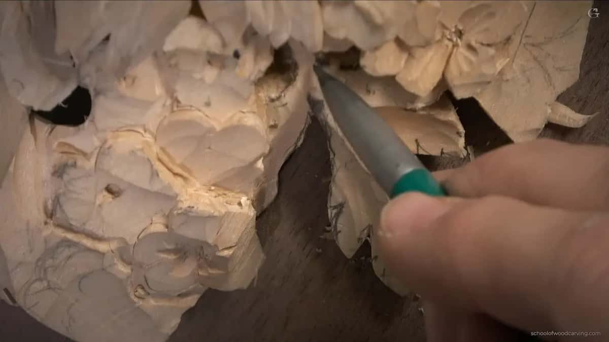A narrow gouge runs down the middle of the leaf between two pencil lines, the fingers of the other hand just in frame