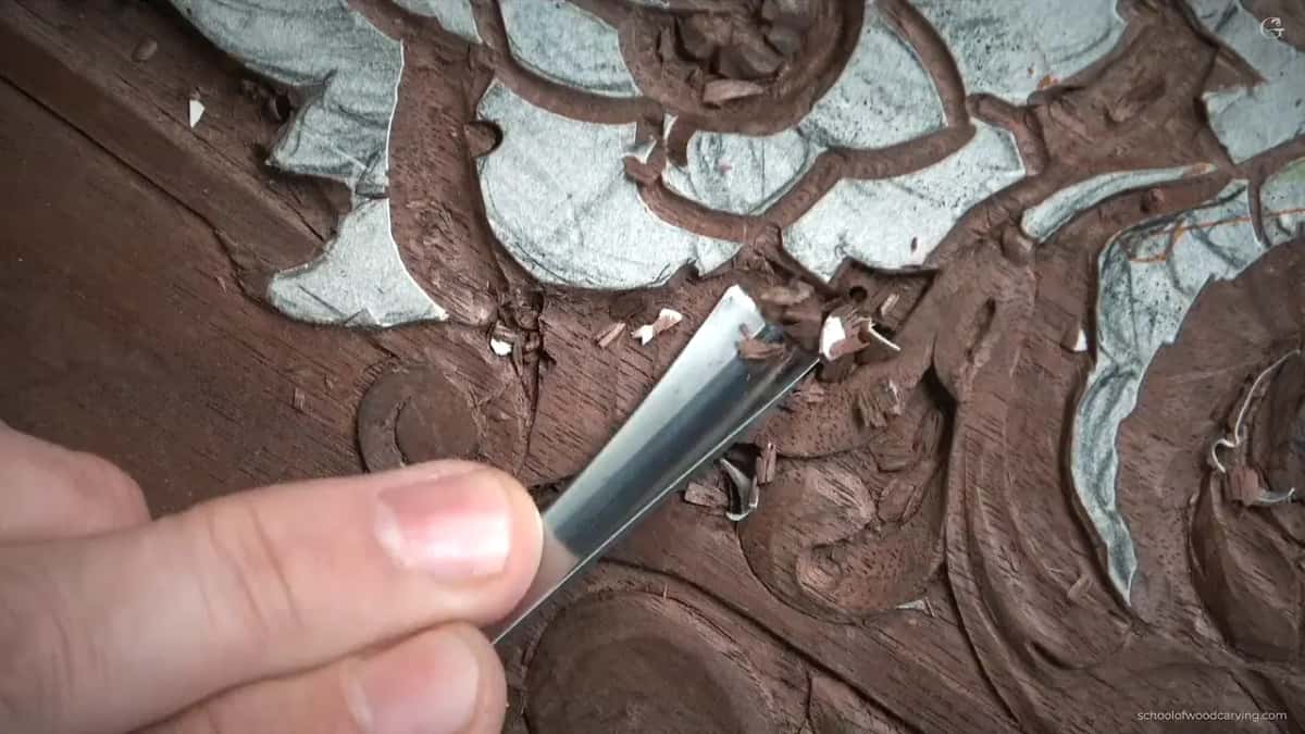 Wide gouge held out over the panel, its edge broad enough to clear a whole hollow in one pass alone.