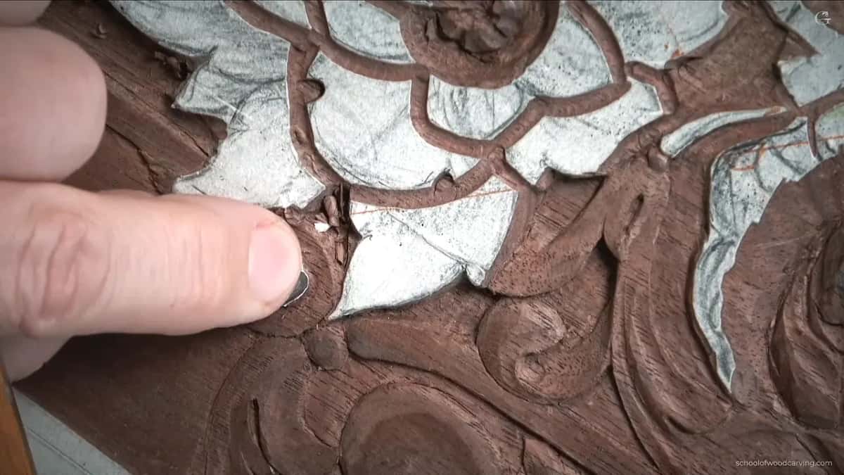 Thumb pressed flat against the carved leaf while the other hand works below.