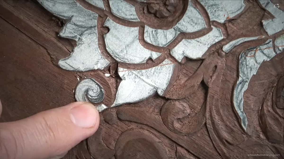 Fingertips resting beside the spiral while the small flat gouge works along its outer turn.
