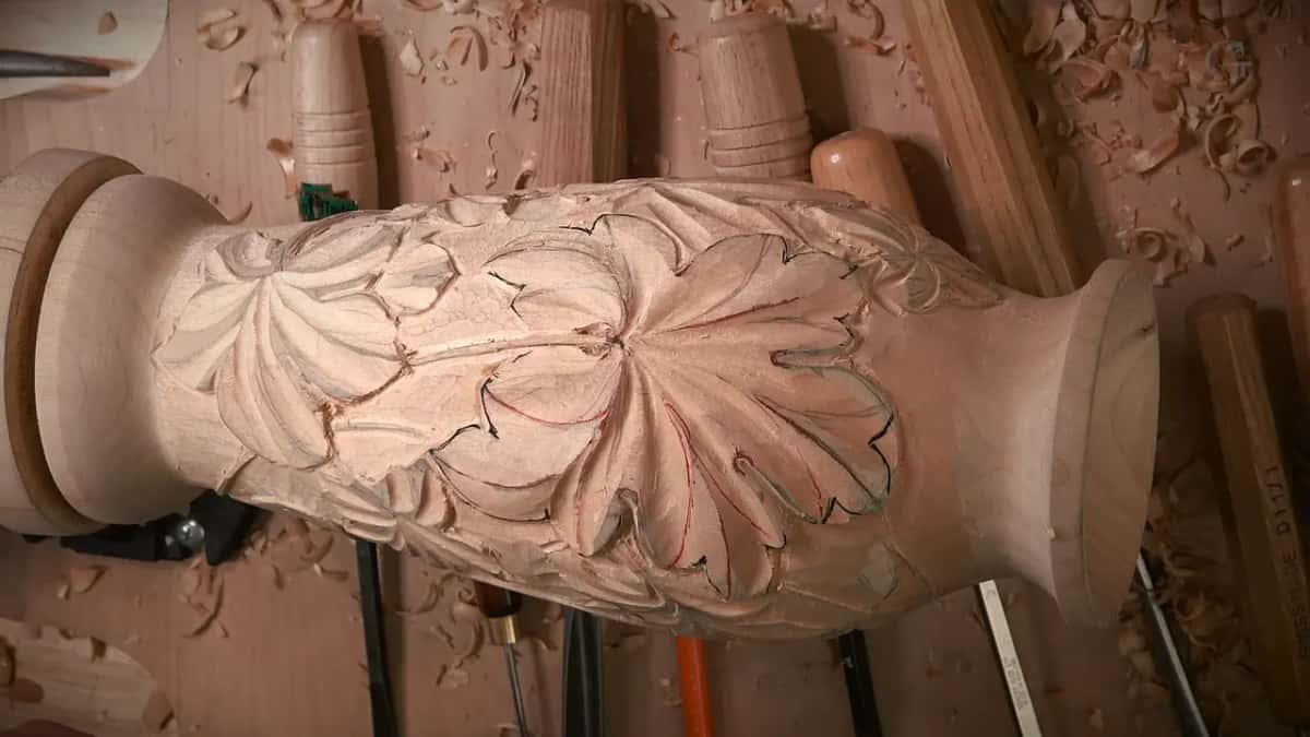 Leaves roughed to shape while the pencil and red layout still shows through, gouges resting behind the vase