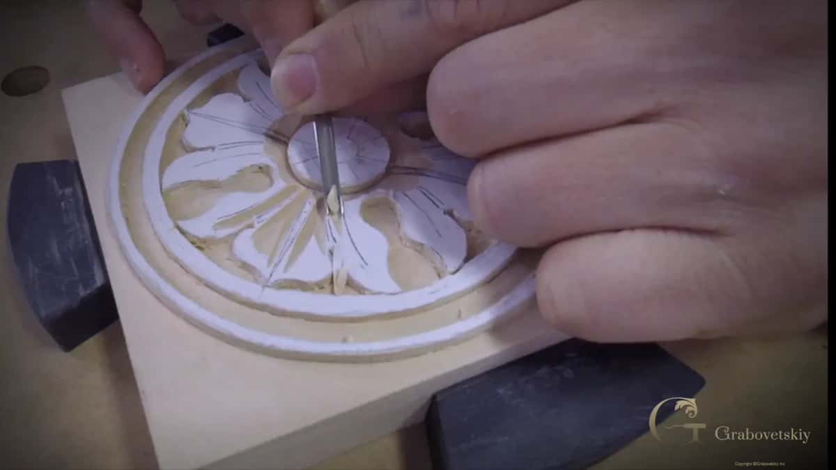 Close on the carved flower, one blade resting in a petal, the rest of the rack spread across the bench below