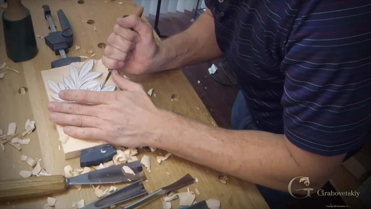 Hands flat on the work, leaf outlined, chips pushed back