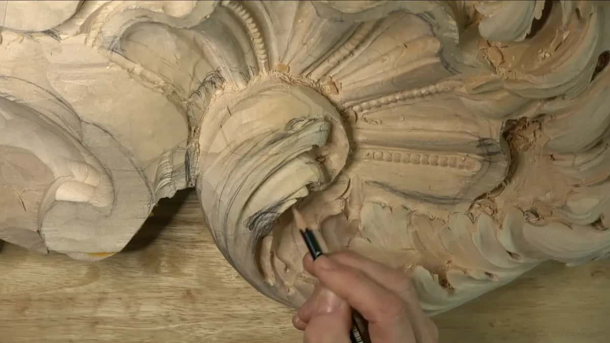 Pencil tip on the curl's inner line, with the shell and its row of beads just above.