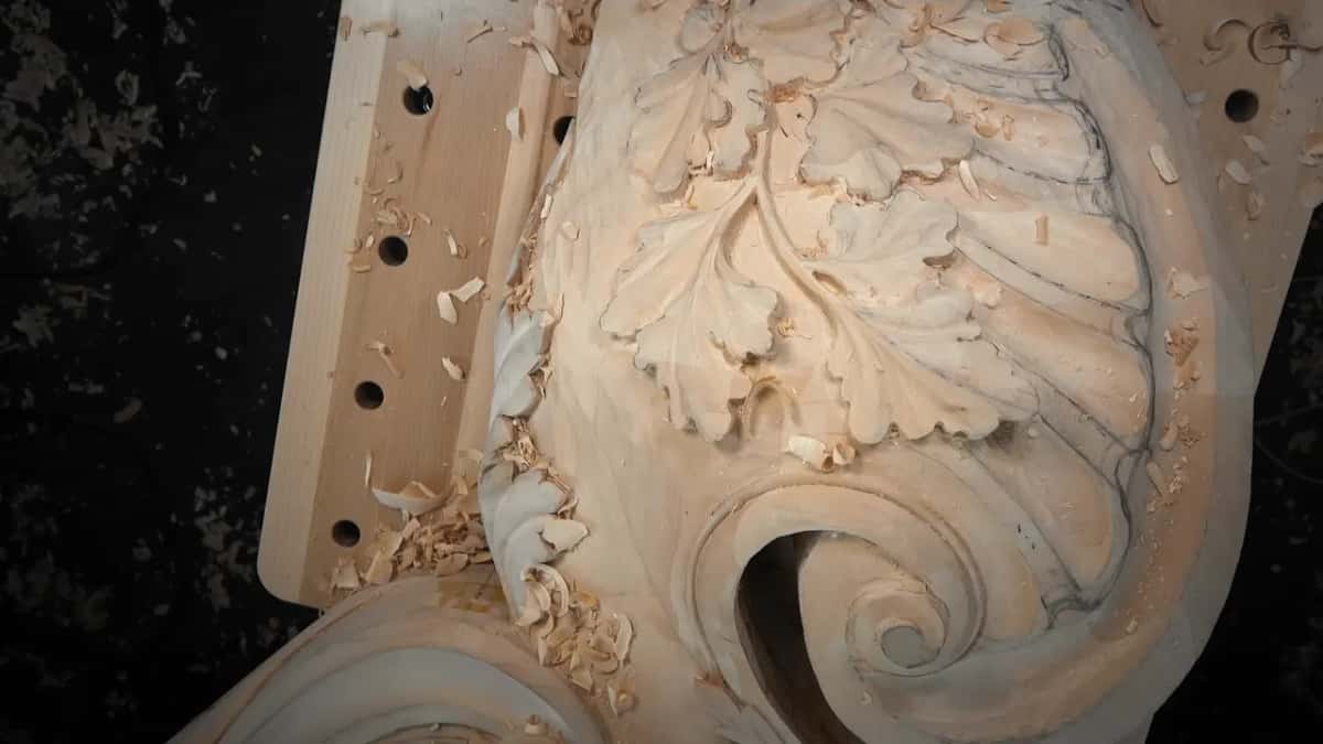 Carved oak leaf above a volute whose opening reads as a solid black shadow against the pale wood