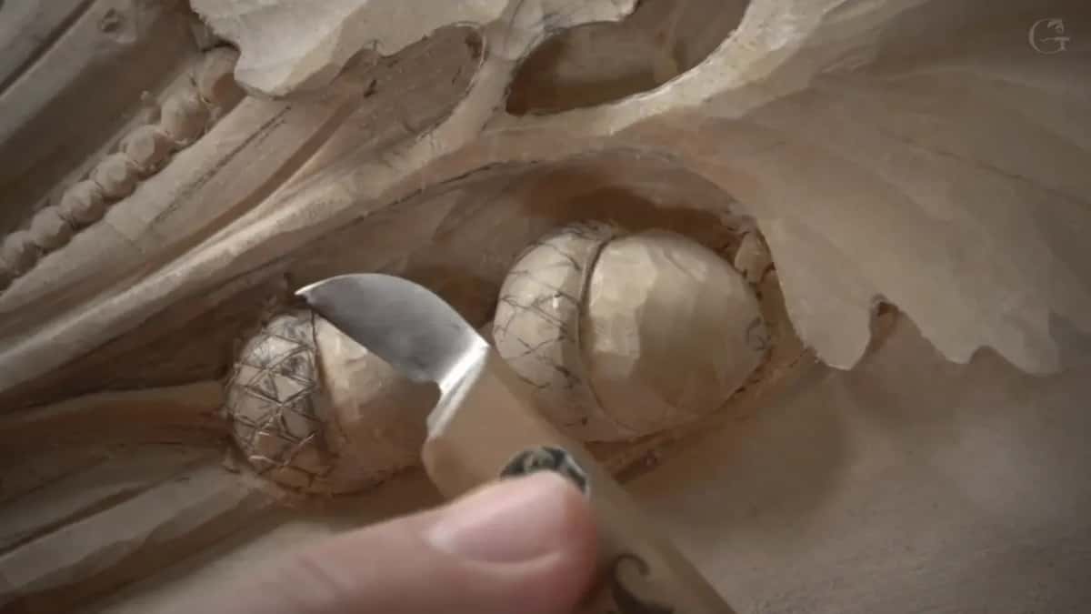 Knife blade angled into the cap of one acorn, while the second acorn beside it already carries its full grid