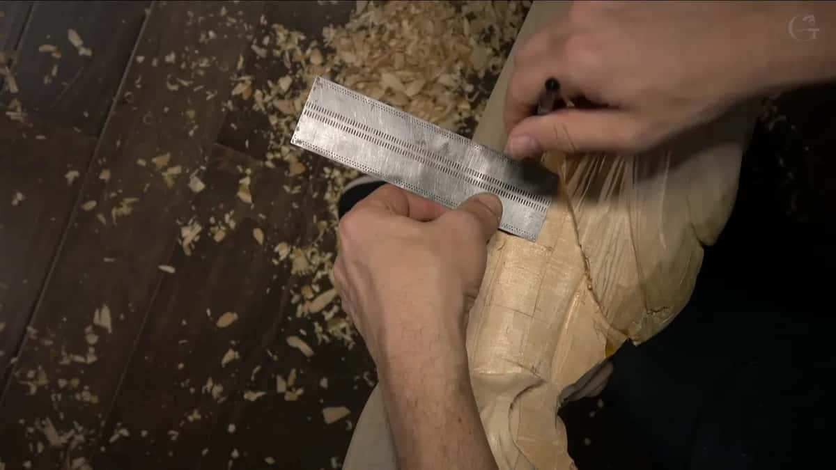 Steel ruler held flat against the carved surface, chips scattered over the dark floor beneath