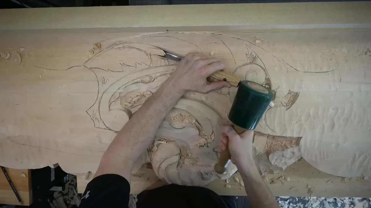 One hand steers the gouge through the upper leaves, the other brings the mallet down.