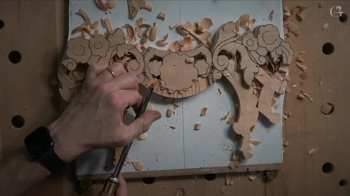 Overhead of the left hand flat on the board, gouge riding on one finger