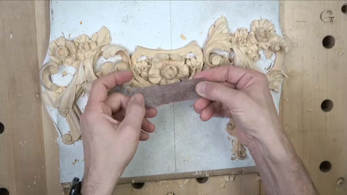 Strip of mesh abrasive stretched between two hands over the finished carving, the open weave letting light through