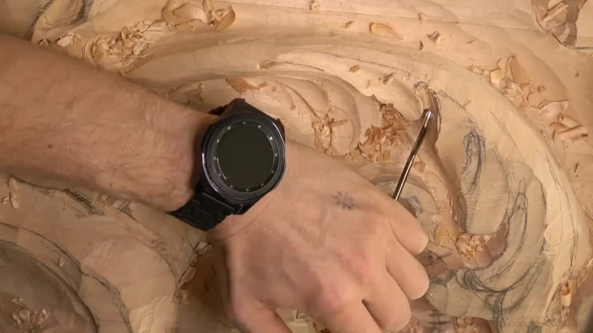 A bent shank tool hooks in under the rolled leaf, the watch and a pile of chips beside it.