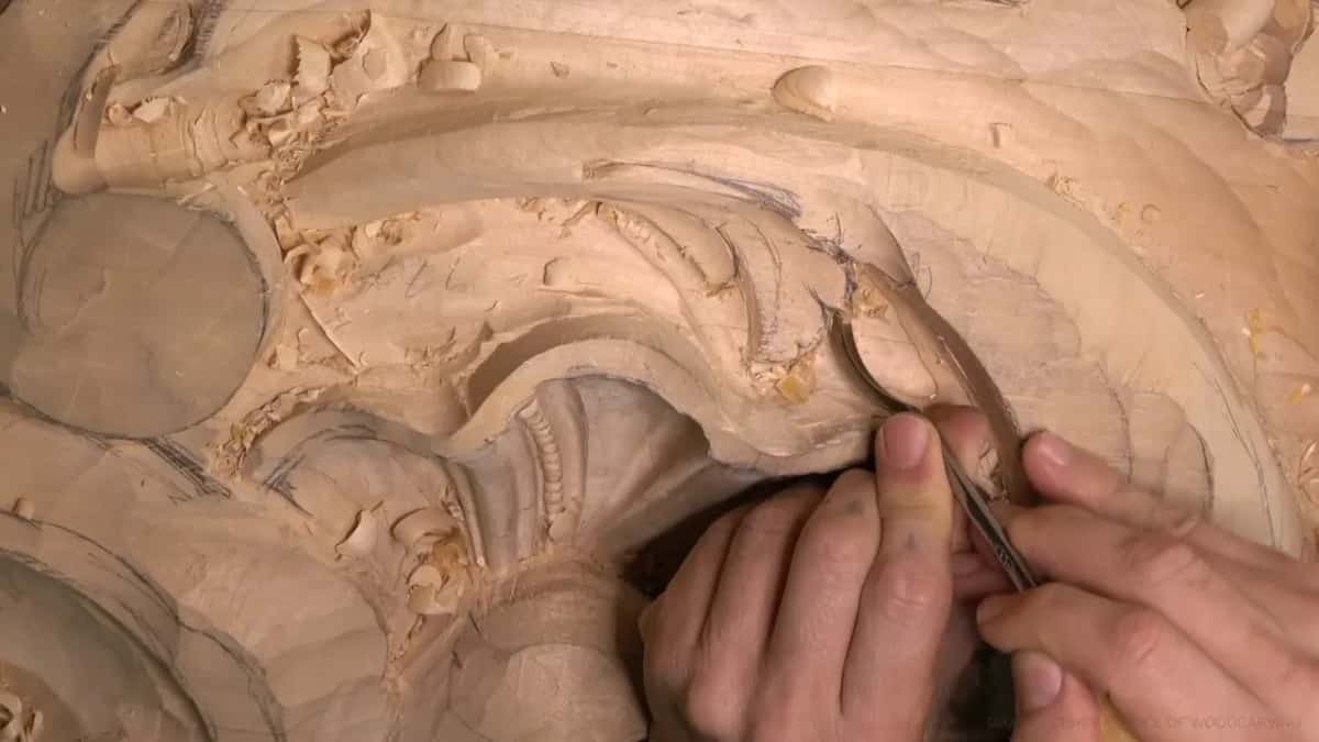 Both hands guide a long, narrow gouge along the rim of the leaf, with pencil lines still showing to the right.