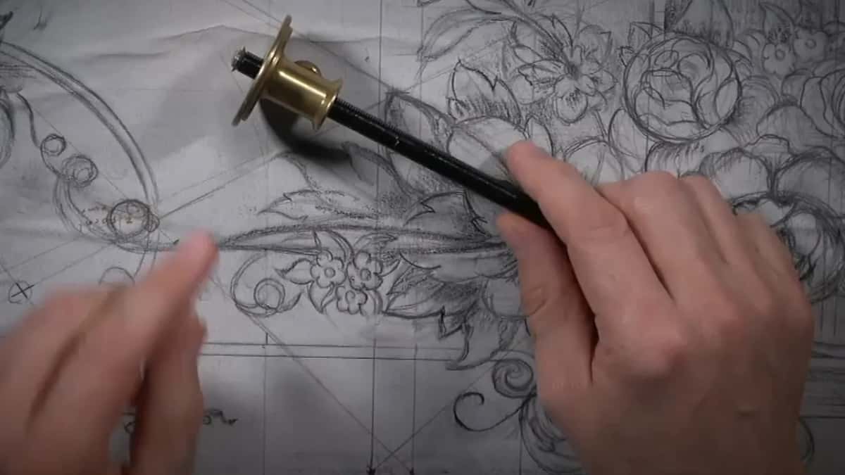 Brass and steel marking gauge lying across the paper drawing, a hand at either side of it