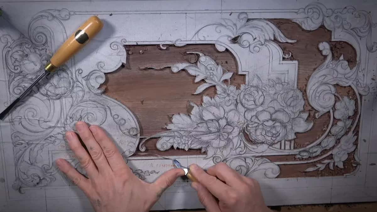 Two hands and a chisel over the board, another tool at the top left