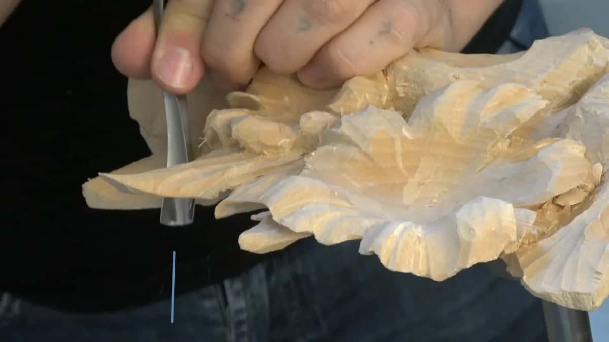 Whole fist around the handle for the deep sweep, the panel turned edge on so the carving runs downhill.
