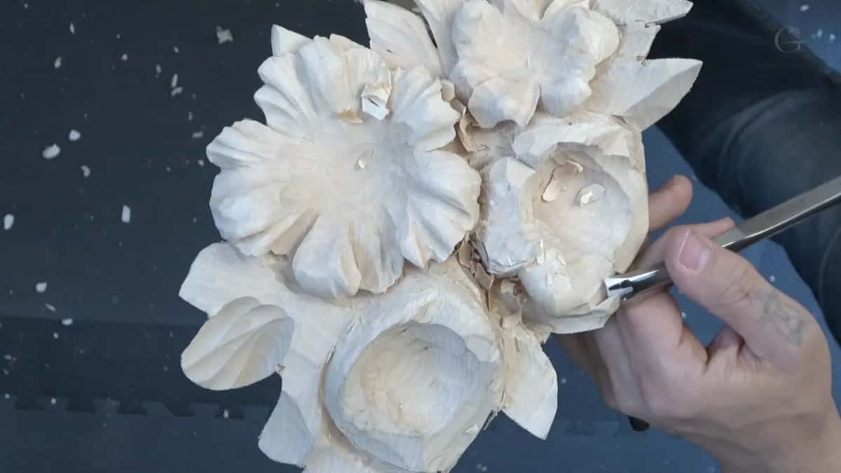 Rolling the petal down and inward with a wider sweep, seen from straight above the bench.