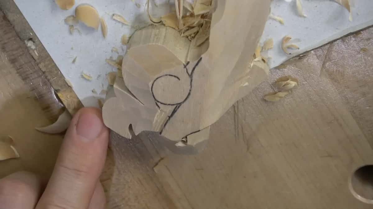 Fingers rest beside the scroll while loose shavings sit on the white ground around it.