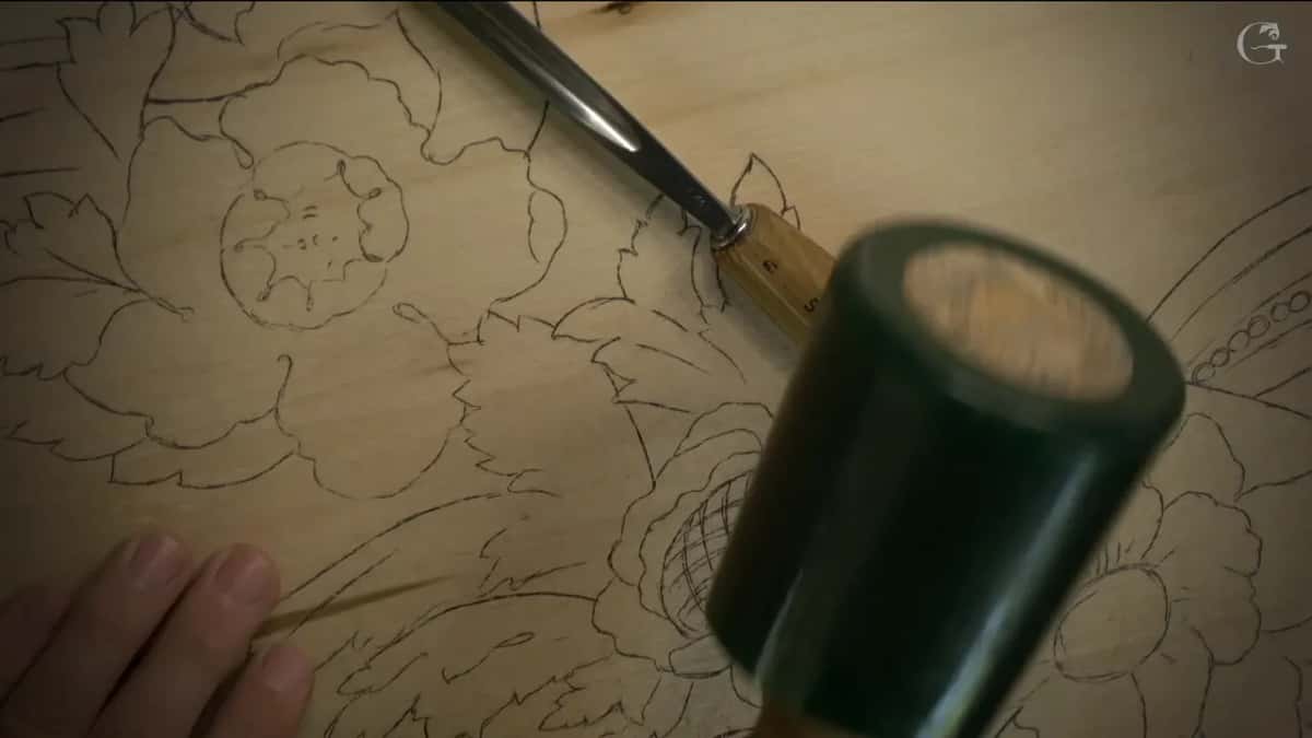 Dark green mallet raised over a gouge set on the pencil flowers