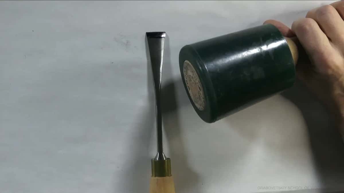 Big green mallet beside a straight chisel