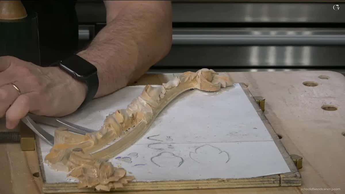 Chisel worked in under the carving, flat against the board.