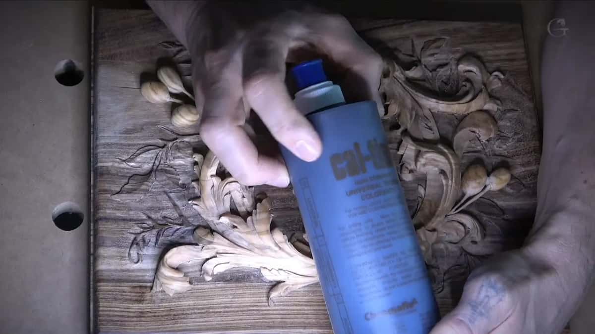 Blue bottle of raw umber Cal-Tint universal tint colorant held over the carving it is about to be blended into