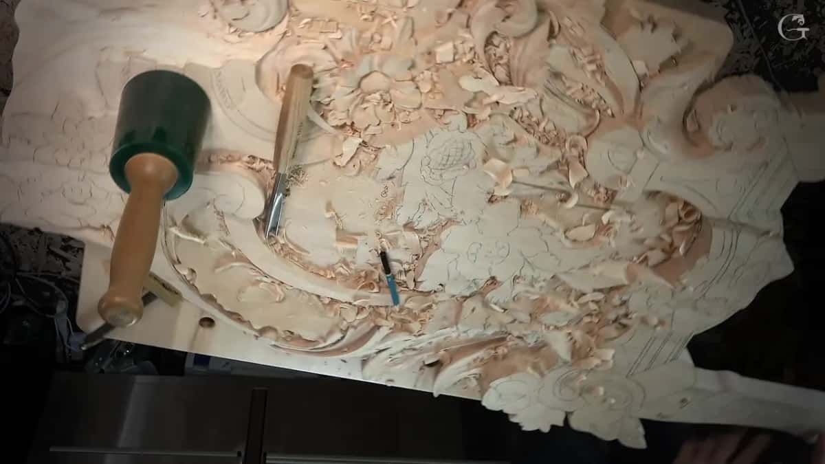 Overhead view of the whole carved panel with a green mallet and a gouge lying across the chips