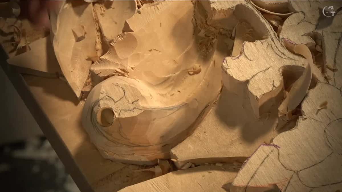Round hole bored clean through the eye of the acanthus scroll, with chips lying loose all around the opening