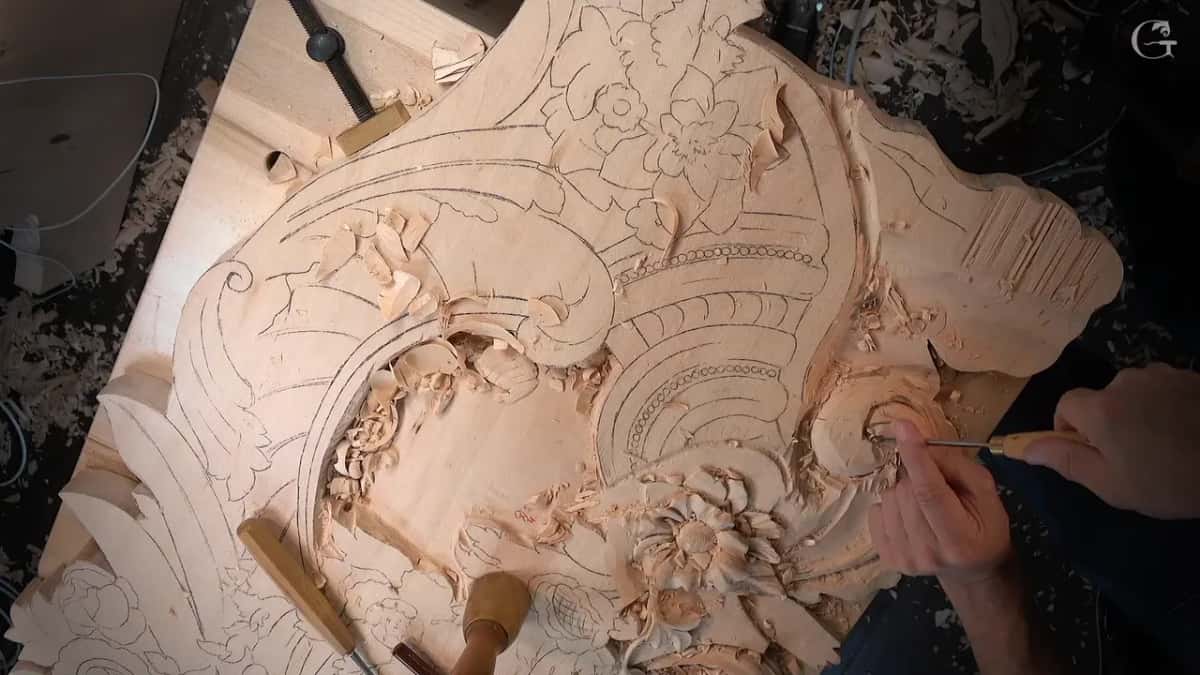 Board clamped to the bench with three gouges and a mallet resting on the uncarved corner