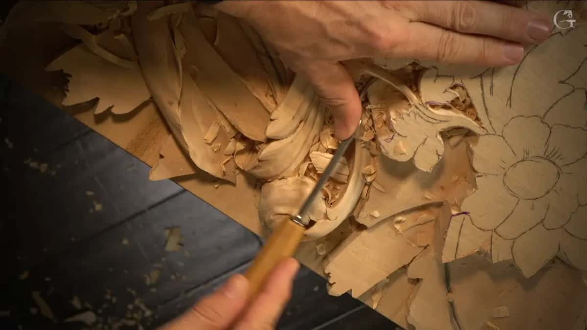 Two hands guiding a long thin blade under a leaf being freed